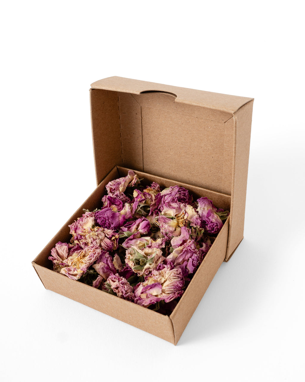An open brown cardboard box filled with dried pink flower petals, photographed on a clean white background.