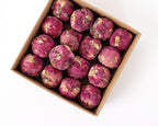 A top-down view of dried rose balls in a brown cardboard box on a white background.