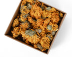 A top-down view of dried orange calendula flowers packed inside a brown cardboard box on a white background.