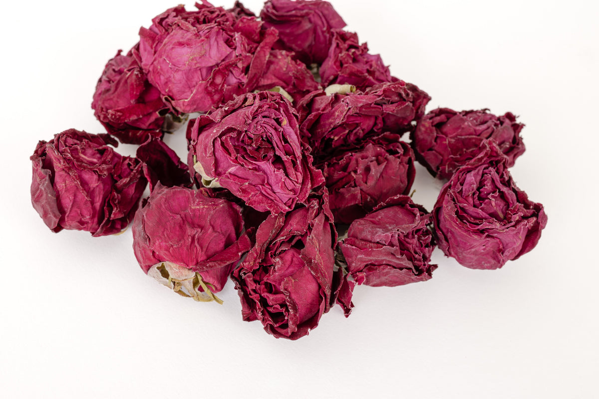 A pile of dried dark pinkish-red roses on a plain white background.