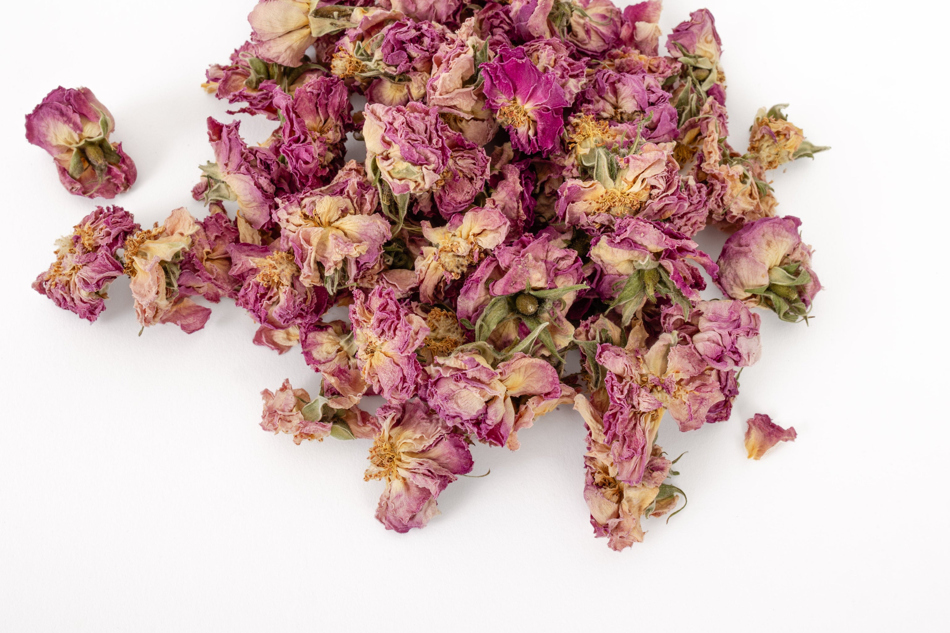 A pile of dried pink rose petals with yellow centers, scattered on a plain white background.