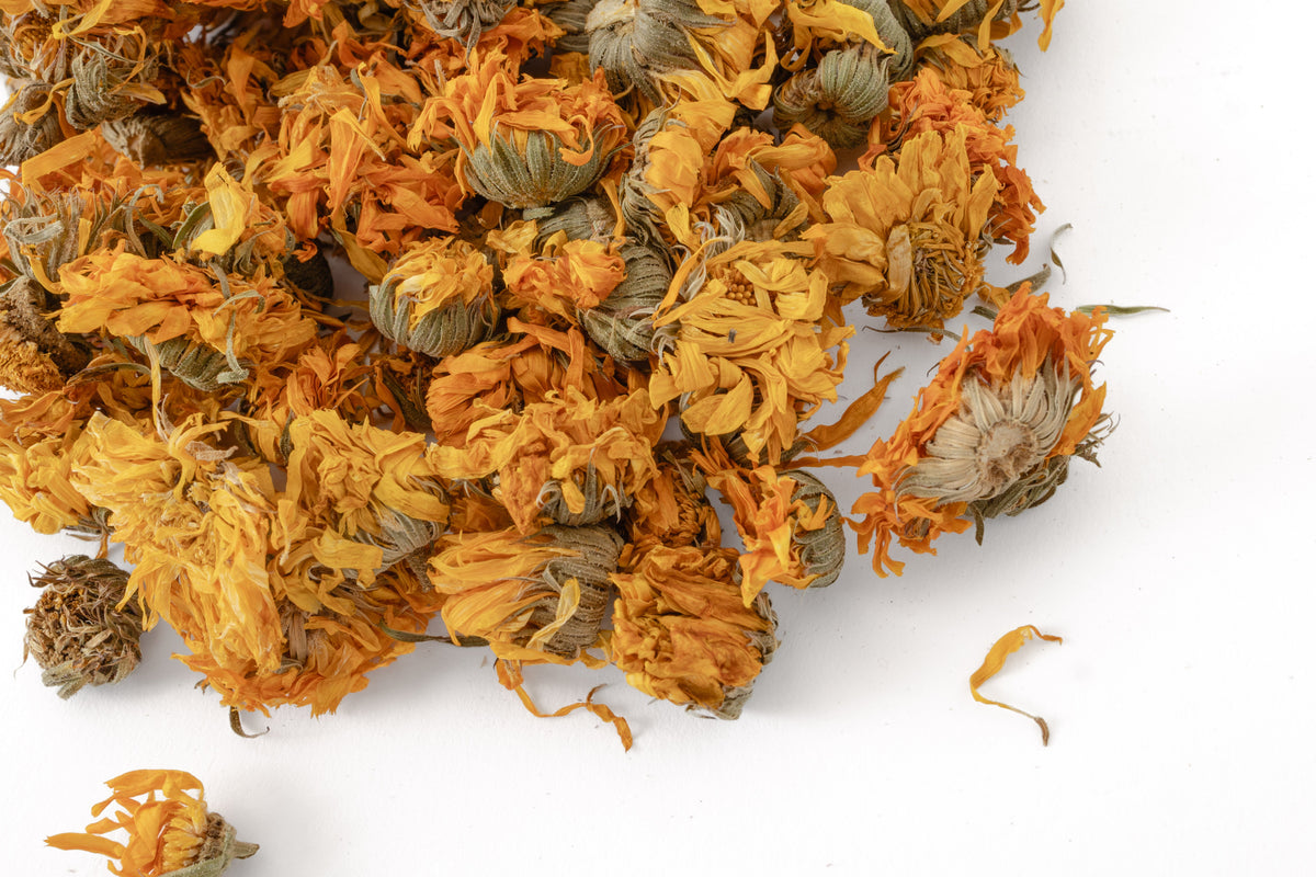 Dried orange calendula flowers scattered on a clean white background.