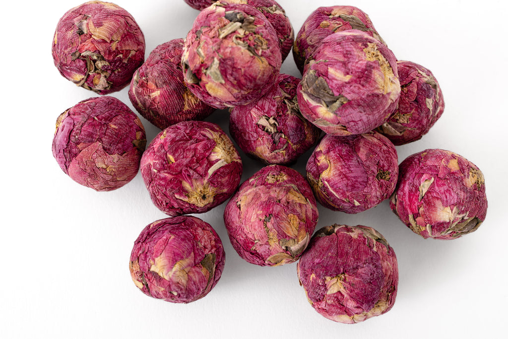 A pile of dried, pinkish-red rose flower buds rolled into a ball, arranged on a clean white background.